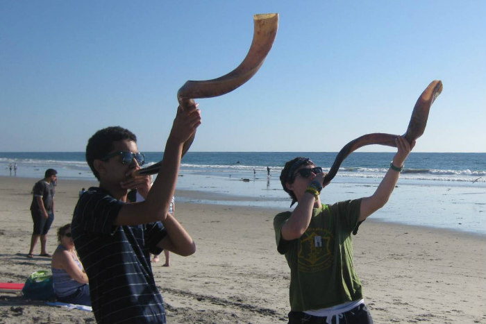Two teenage boys blowing shofars on a beach