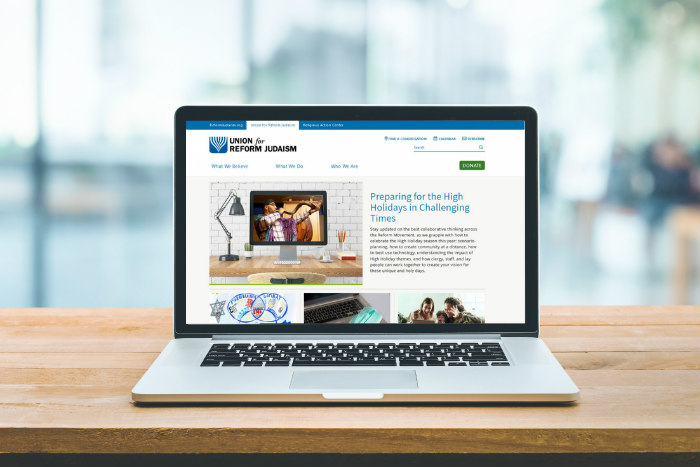 Laptop sitting on a wooden surface displaying the newly redesigned URJ website 