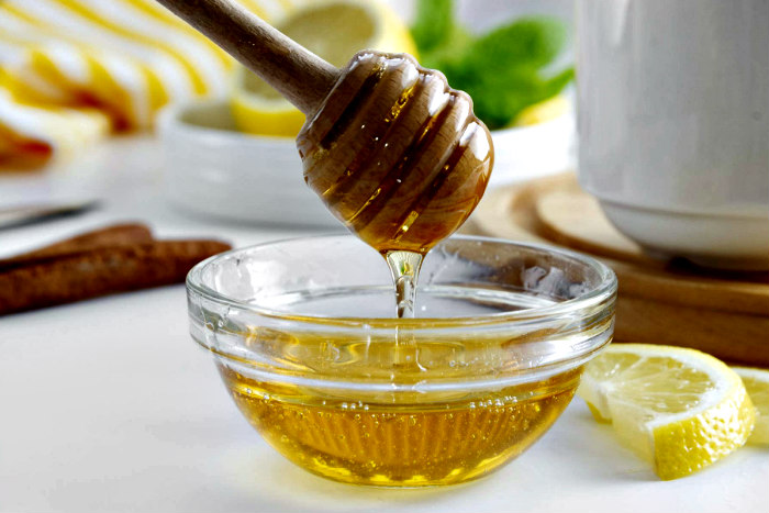 Honey dipper dripping honey over a small glass bowl of honey