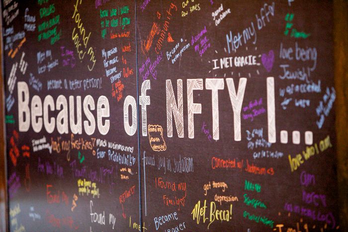 Chalkboard sign reading BEACUSE OF NFTY I surrounded by answers scrawled in colorful chalk 