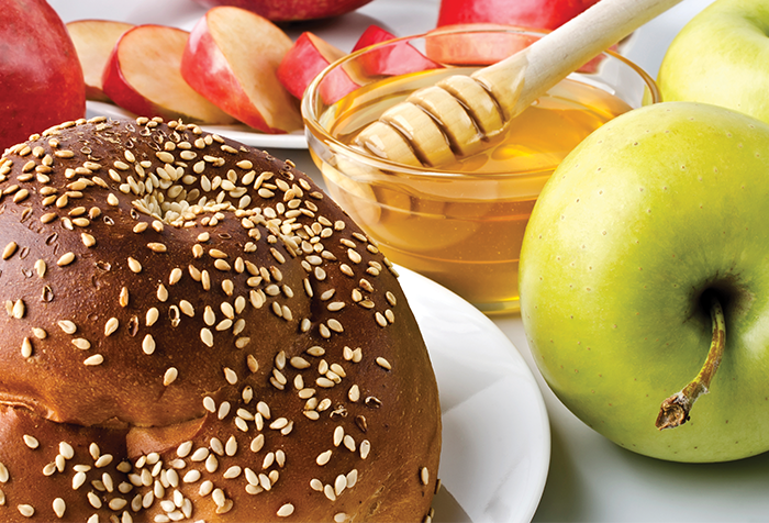 A table with sliced apples, a bowl of honey with a wand, and a round challah.