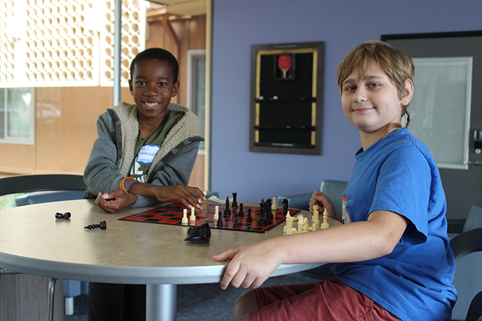 two campers playing chess and smiling at the camera