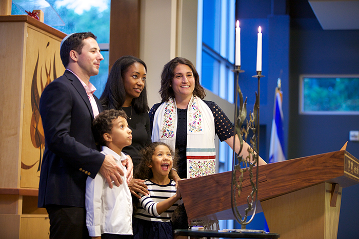 an image of an Interracial family of four standing on the bema at a synagogue with the rabbi