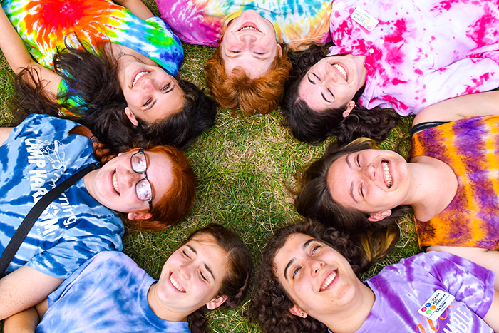 an image of 7 campers at 6 Points Art Camp laying in a circle, each one wearing a colorful tie dye shirt