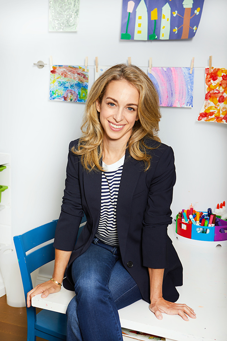 Dr. Becky Kennedy, a clinical psychologist and bestselling author, sitting on a kid-size table in front of a white wall covered in kids' art