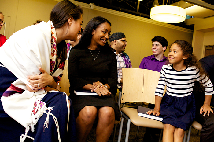 an image of a woman wearing a tallit talking to a mother and her daughter at services