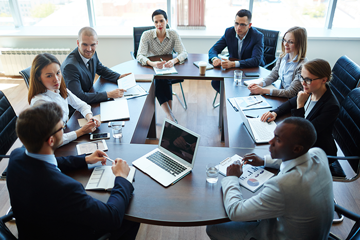 Photo of 8 men and women wearing suits sitting around a table in an office