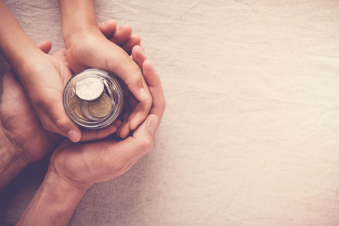 Photo of two sets of hands holding a jar full of coins
