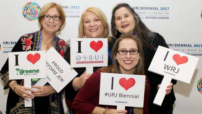 Smiling people holding Reform Movement related signs against a URJ Biennial backdrop 