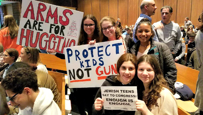 Teens holding signs reading ARMS ARE FOR HUGGING and PROTECT KIDS NOT GUNS