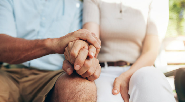 Closeup of seated middle aged man and woman holding hands 
