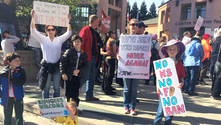 Group of people holding various handmade signs welcoming and supporting refugees