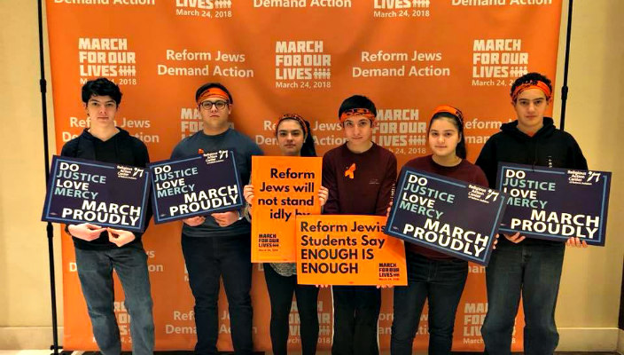 Group of teens holding signs for gun violence prevention in front of an orange March for Our Lives banner