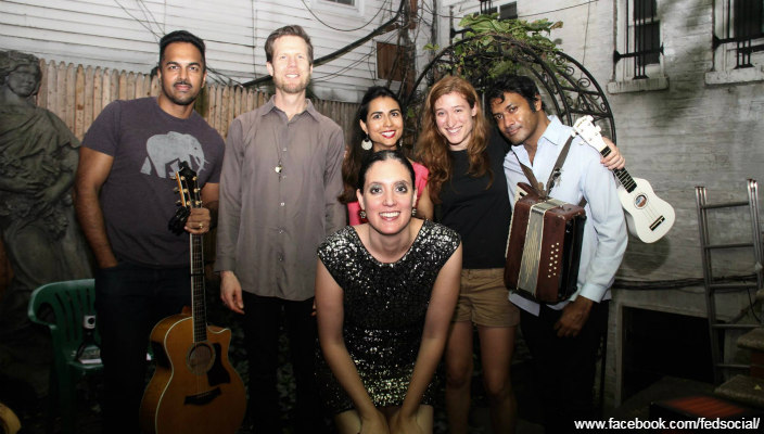 Group of people of varying ethnicities standing together and smiling outdoors while holding instruments as at an event or party