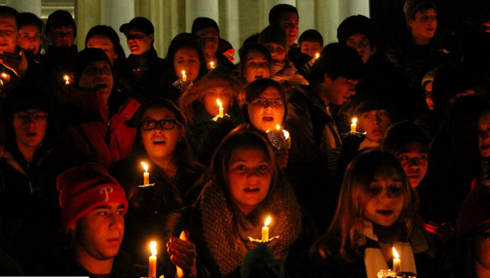Lighted faces of teenagers holding candles in the dark