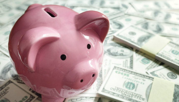 Pink piggy bank sitting atop piles of money