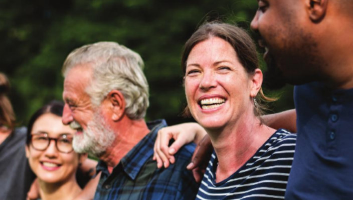 Smiling people of various ages genders and races with their arms around one another 