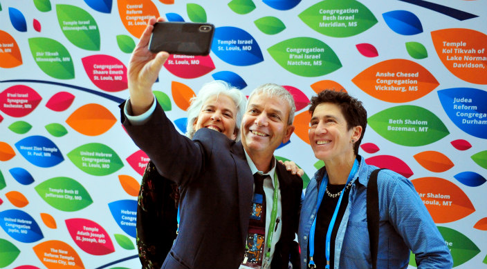People taking a smiling selfie in front of a Biennial backdrop