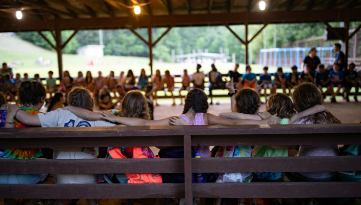 Young campers facing away from the camera with their arms around one anothers shoulders