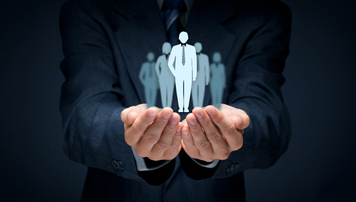 Man in dark business suit holding small cardboard silhouettes of people in his outstretched hands