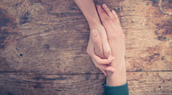 Two people's right hands clasped in a show of empathy or support