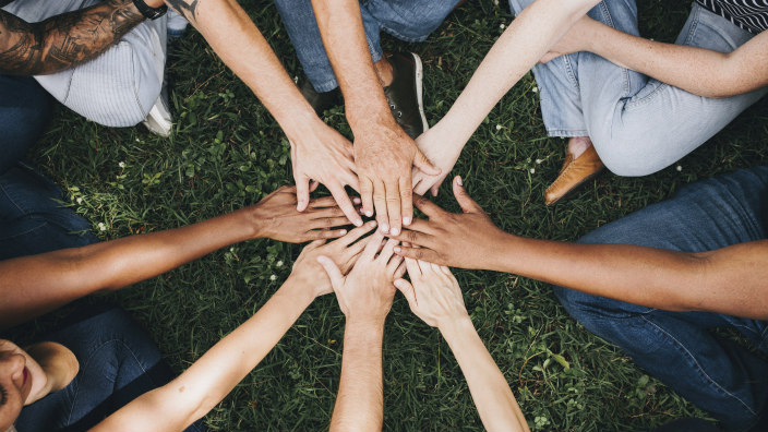 Many people sitting in a circle on the grass with their hands in the middle 