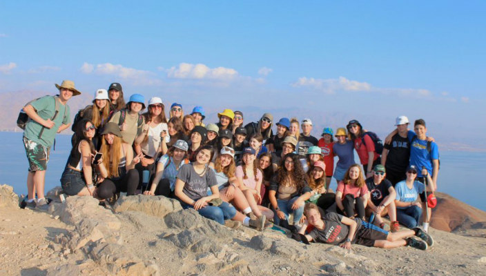 Smiling group of teenagers on a sand dune in Israel with a blue sky behind them 