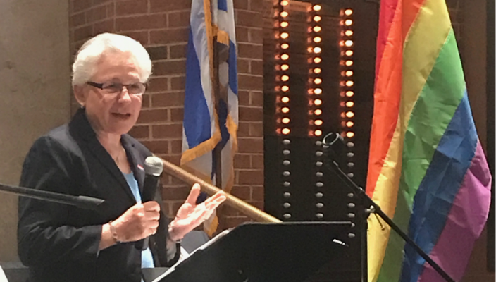 The author on the bimah at her congregation. The Pride flag is visible in front of her, the Israeli flag behind her.