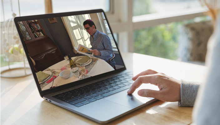 Womans hand on a laptop keyboard with a seder playing on the computer screen