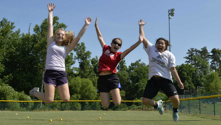 Three campers in mid-air jumps on a grassy field