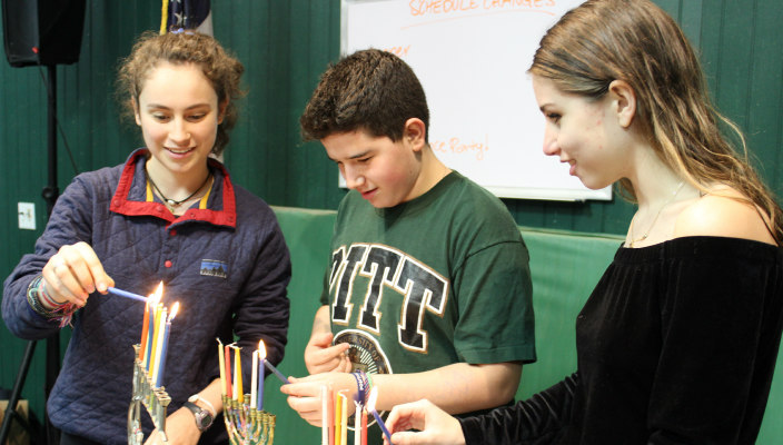 Three students lighting hannukiot