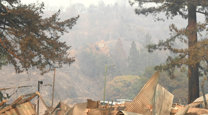 Charred remains of the physical location of URJ Camp Newman beneath hazy skies with mountains in the background and a painted Star of David still visible on them