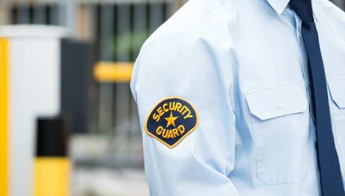 Male security guard with patch on the sleeve of his white shirt and a tie; his head is not visible.