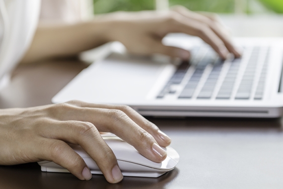 a hand clicking a mouse while the other hand types on a keyboard