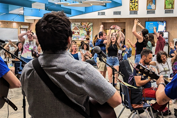 an image of a song leader playing the guitar in front of a room of people singing