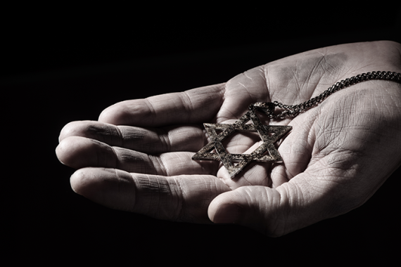 Photo of a closeup of an old and rusty pendant in the shape of the star of david on the hand of a man