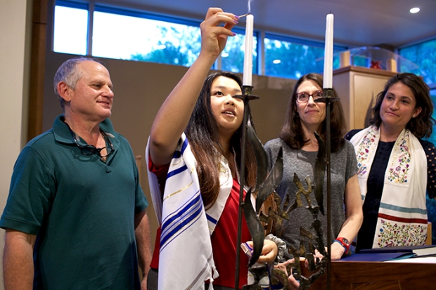 a family lights the Shabbat candles in a synagogue with the clergyperson looking on