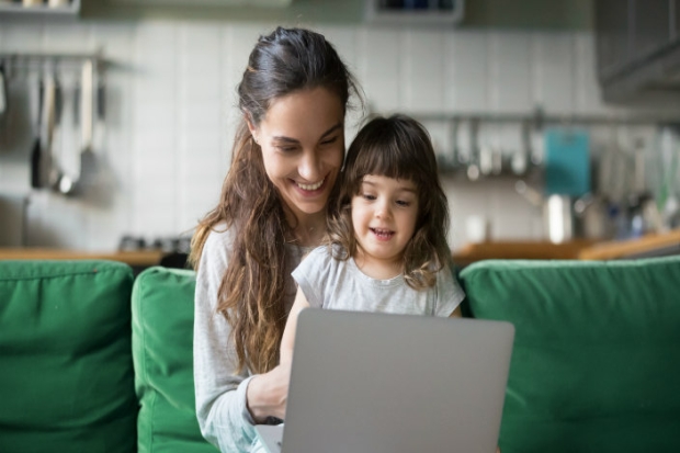 Mom holding daughter on her lap while they look at a laptop from the sofa