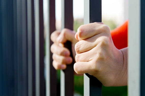 Female hands dressed in orange holding onto prison bars 