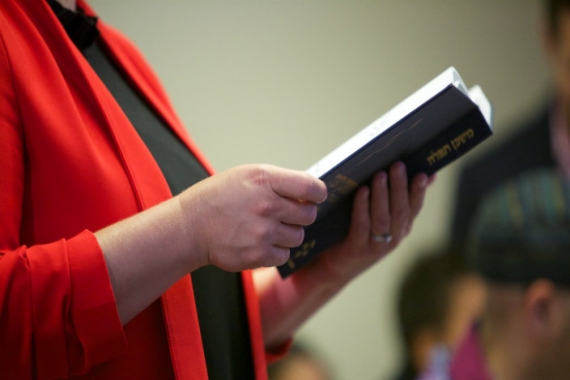 Side view of a standing woman holding an open prayerbook