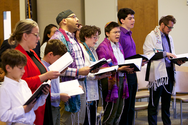 group of people standing and holding prayer books and wearing tallit