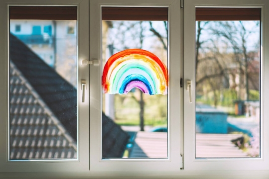 Three pane window with a rainbow fingerprinted onto it and facing the outdoors