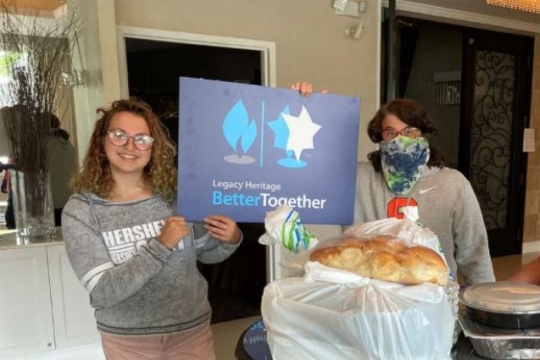 A young woman and an older woman standing together holding a challah and a BETTER TOGETHER sign