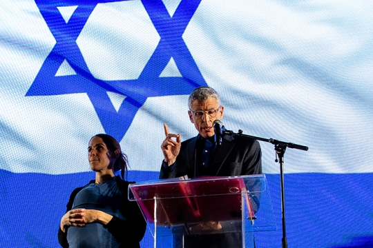 Rabbi Rick Jacobs addressing protest with a sign language interpreter at his side and the flag of Israel displayed behind him