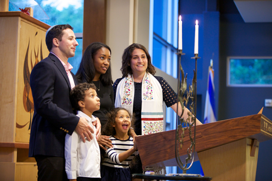 an image of an Interracial family of four standing on the bema at a synagogue with the rabbi