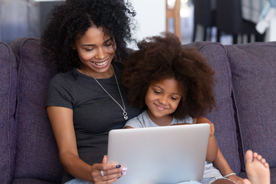 an image of a woman with a child sitting on a sofa looking at computer screen