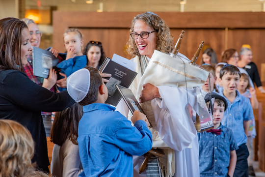 an image of a woman holding a Torah during the High holiday service while people touch the Torah with their prayer book