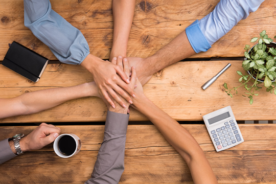 Photo of 6 arms/hands in the middle of a team huddle