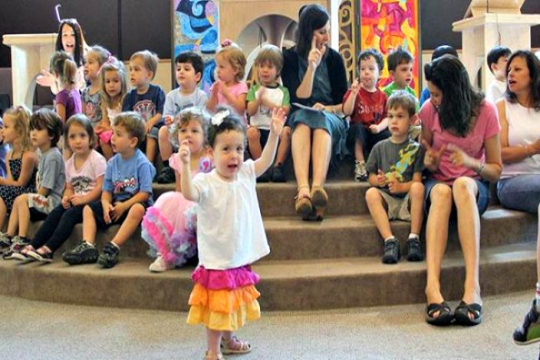 Toddler at synagogue programming with arms raised as if dancing 