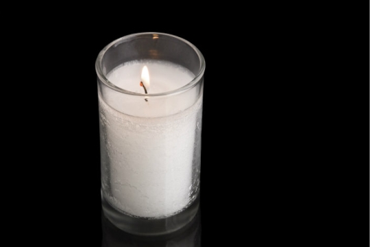 Unlit white memory candle in a glass votive against a black backdrop 
